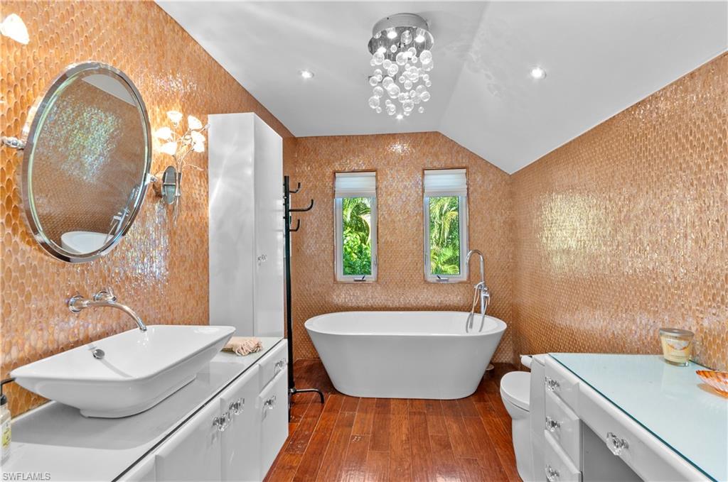 en-suite Bathroom with vanity, vaulted ceiling, dark wood-style flooring, a freestanding tub, and a chandelier