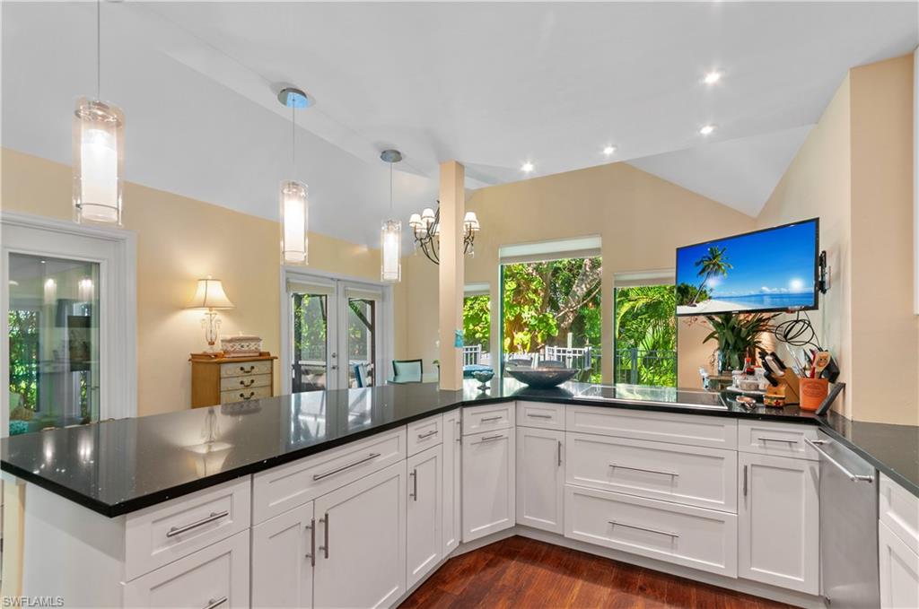 Kitchen with vaulted ceiling, hanging light fixtures, dark stone countertops, dark wood-type flooring, and white cabinetry