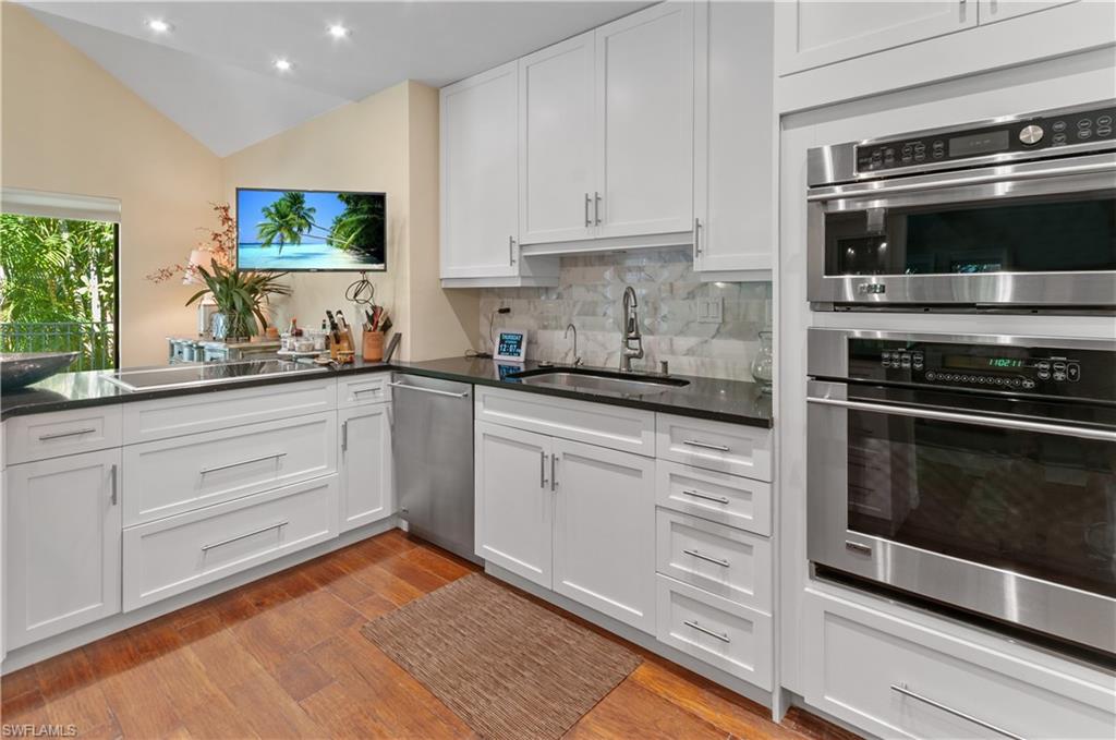 Kitchen with appliances with stainless steel finishes, lofted ceiling, white cabinets, light wood finished floors, and dark stone counters
