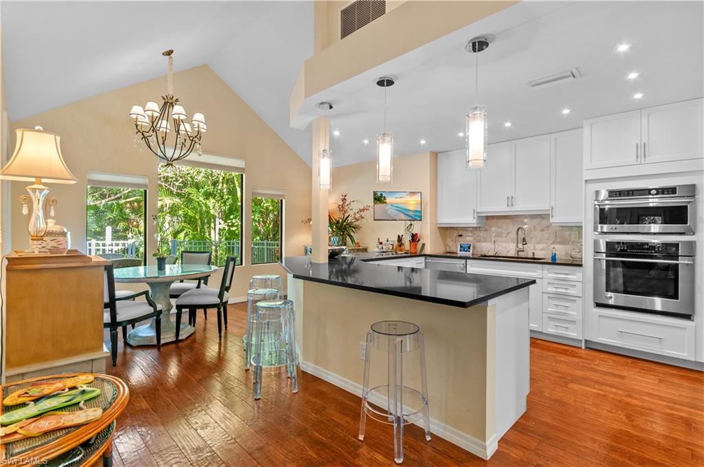 Kitchen with a kitchen breakfast bar, decorative light fixtures, decorative backsplash, white cabinetry, and high vaulted ceiling