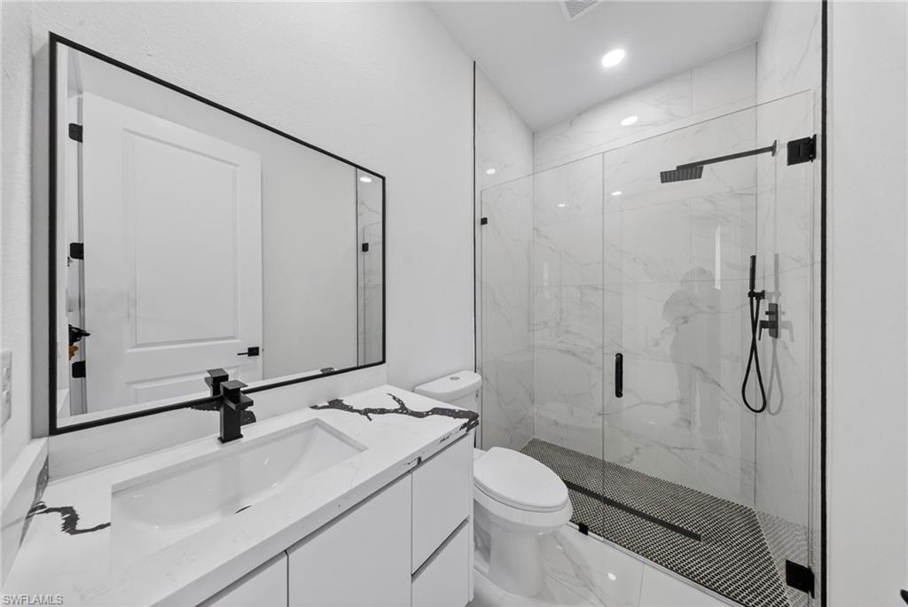 Modern bathroom featuring a floating vanity with rectangular vessel sink and quartz countertop, large framed mirror with matte black hardware, frameless glass shower enclosure with subway tile surround and linear drain, and white cabinetry with integrated storage
