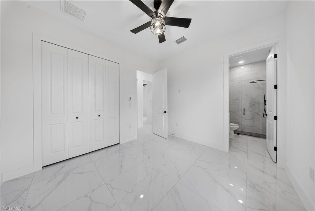 Spa-inspired primary ensuite featuring polished stone-finish flooring, a frameless glass-enclosed shower with tile surround, ceiling fan with integrated lighting, and multiple white panel doors providing ample storage and privacy