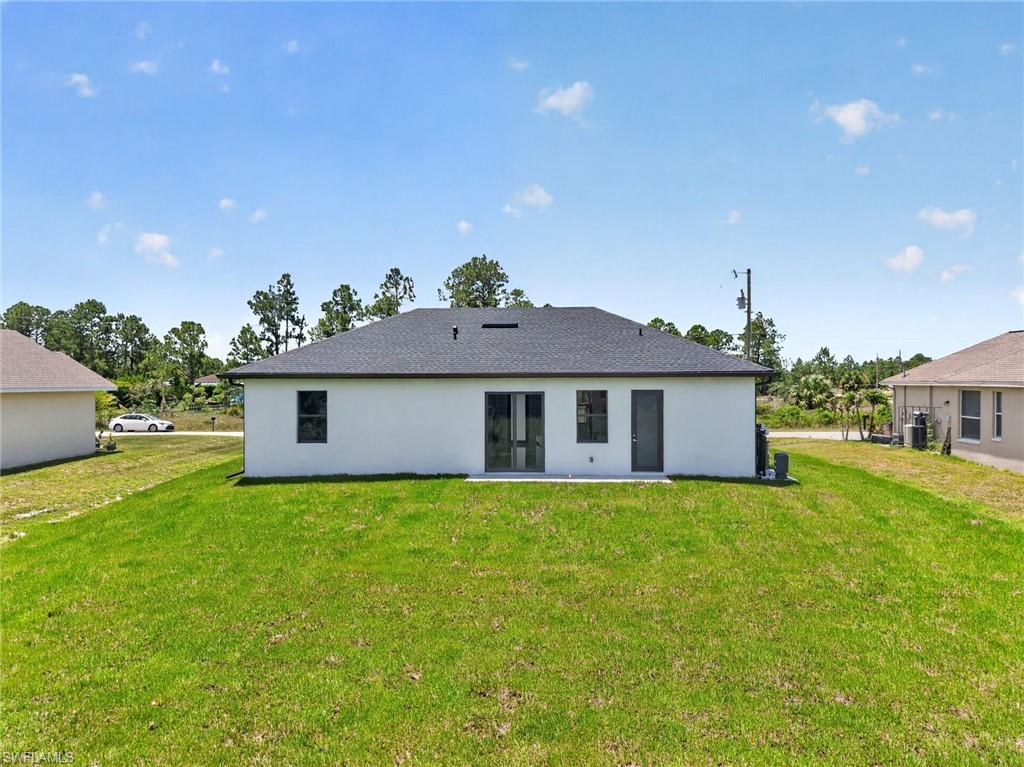 Modern white exterior with dark gray asphalt shingle roof, featuring multiple glass-panel doors and windows, set on expansive manicured lawn with mature trees throughout the property and neighboring residences visible in the distance