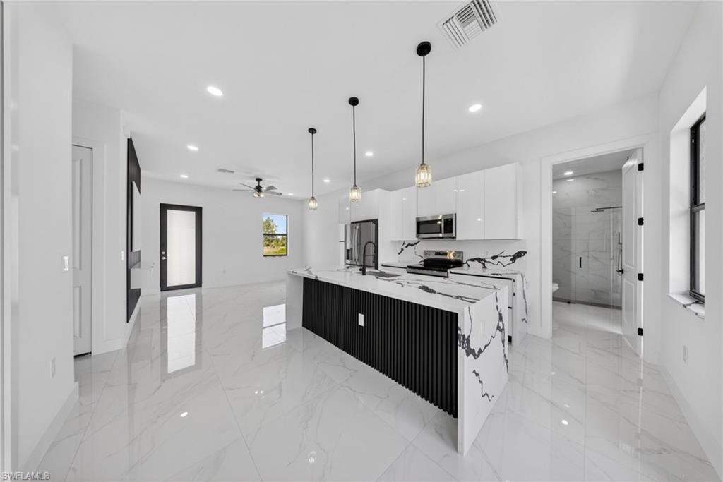 Open-concept layout featuring polished tile flooring, a kitchen island with stone countertops, white cabinetry, and recessed lighting throughout