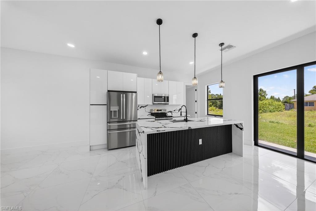 Modern kitchen featuring white cabinetry, stainless steel appliances, and a striking black-accented island with pendant lighting