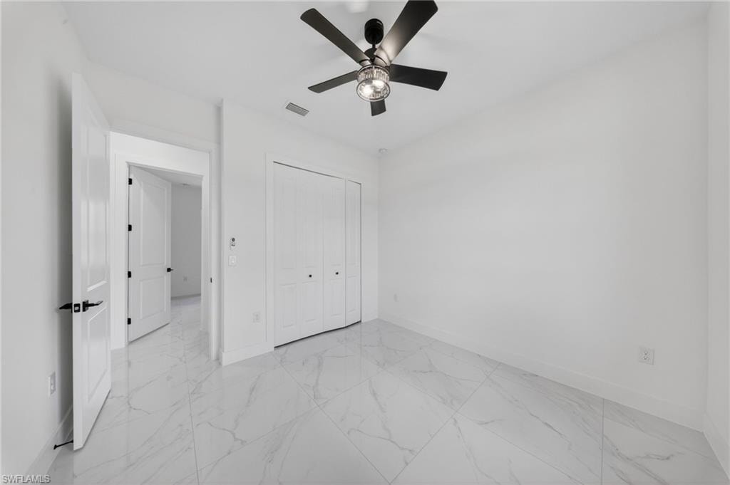 White tile flooring, white walls, white paneled doors, black ceiling fan with integrated lighting, and white bi-fold closet doors