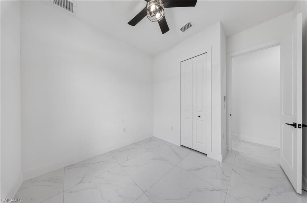 Bright, light-filled bedroom with polished marble-finish flooring, multiple closet entries, and ceiling fan with integrated lighting fixture