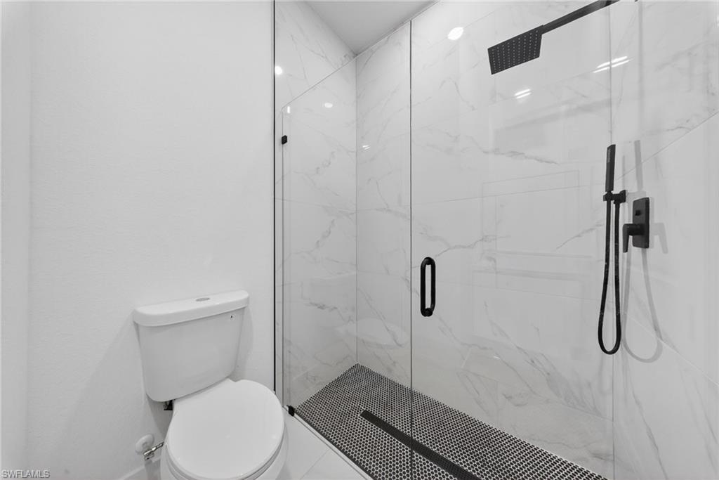 Walk-in shower with clear glass enclosure, matte black fixtures, and white marble-patterned tile