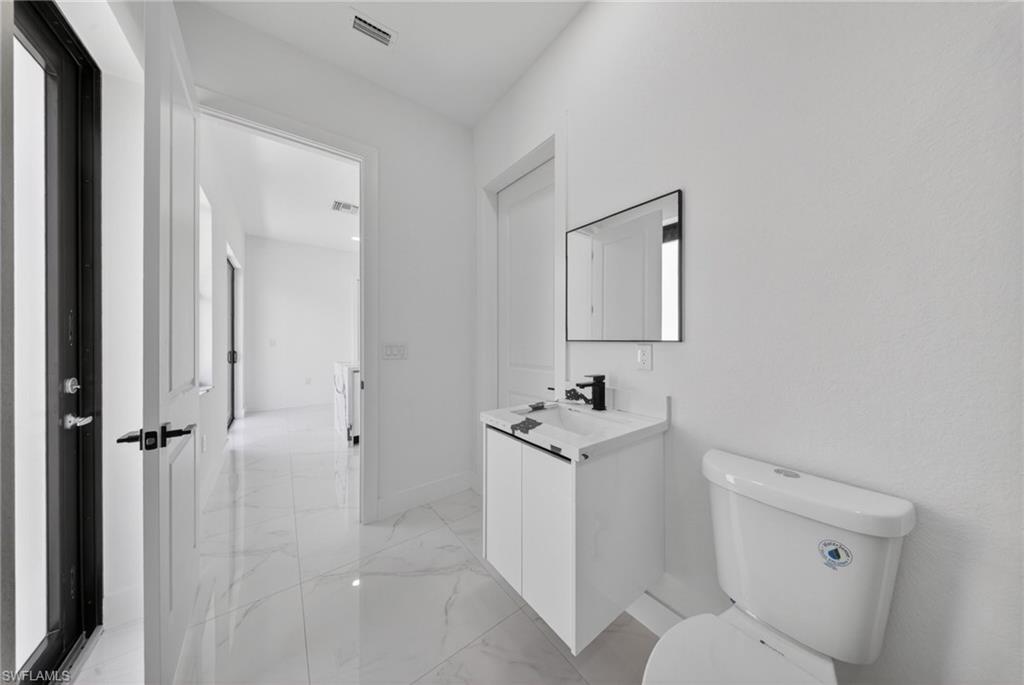 Modern bathroom featuring a white vanity with integrated sink and matte black faucet, large framed mirror, ceramic tile flooring, and a contemporary toilet with dual flush capability