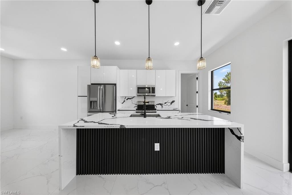 Contemporary kitchen featuring a waterfall-edge quartz island with black vertical slat cabinetry, stainless steel appliances including a built-in microwave, polished porcelain tile flooring, recessed ceiling lighting, and three pendant fixtures with metal and glass accents suspended above the countertop workspace