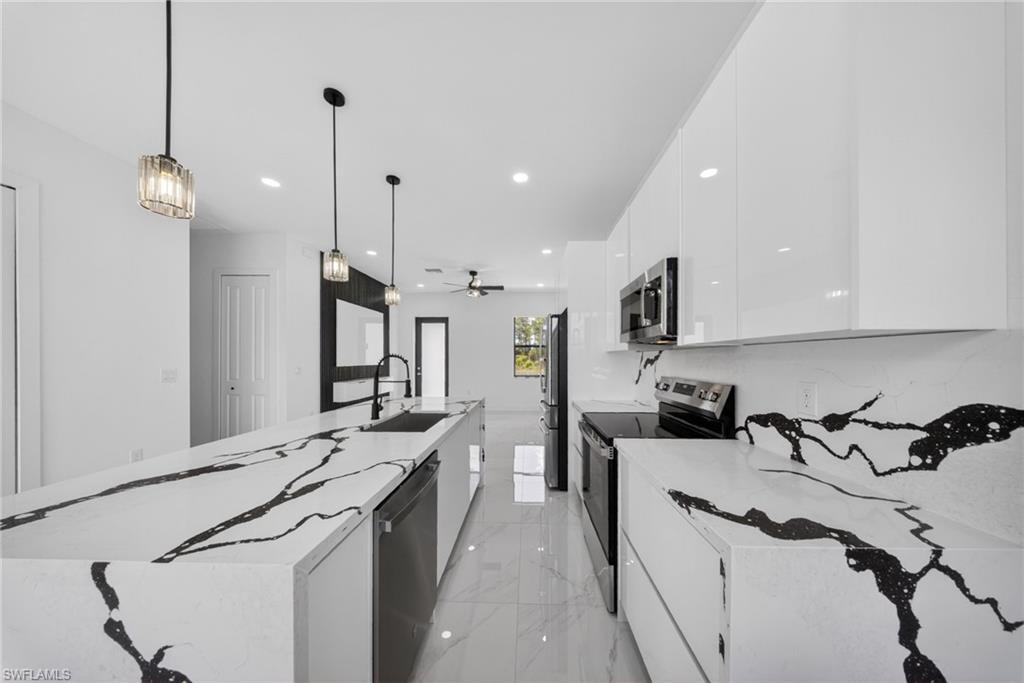 Sleek kitchen featuring white cabinetry, black and white patterned countertops, stainless steel appliances, and pendant lighting