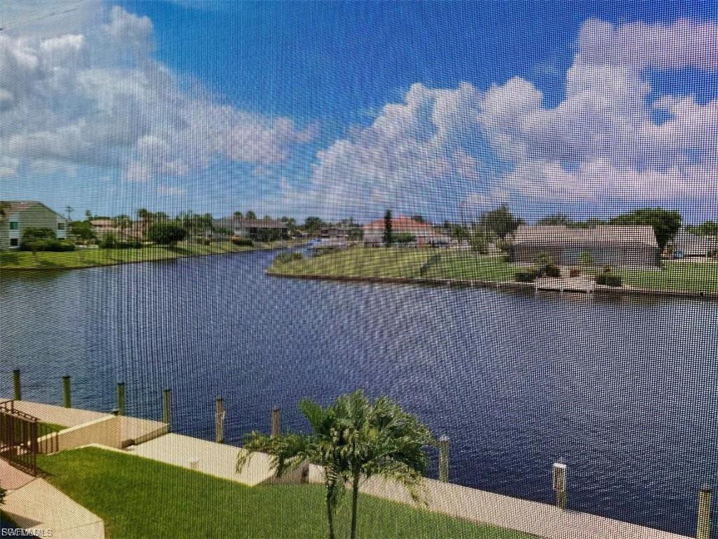 Waterfront property featuring a canal, mature palm trees, and a manicured lawn
