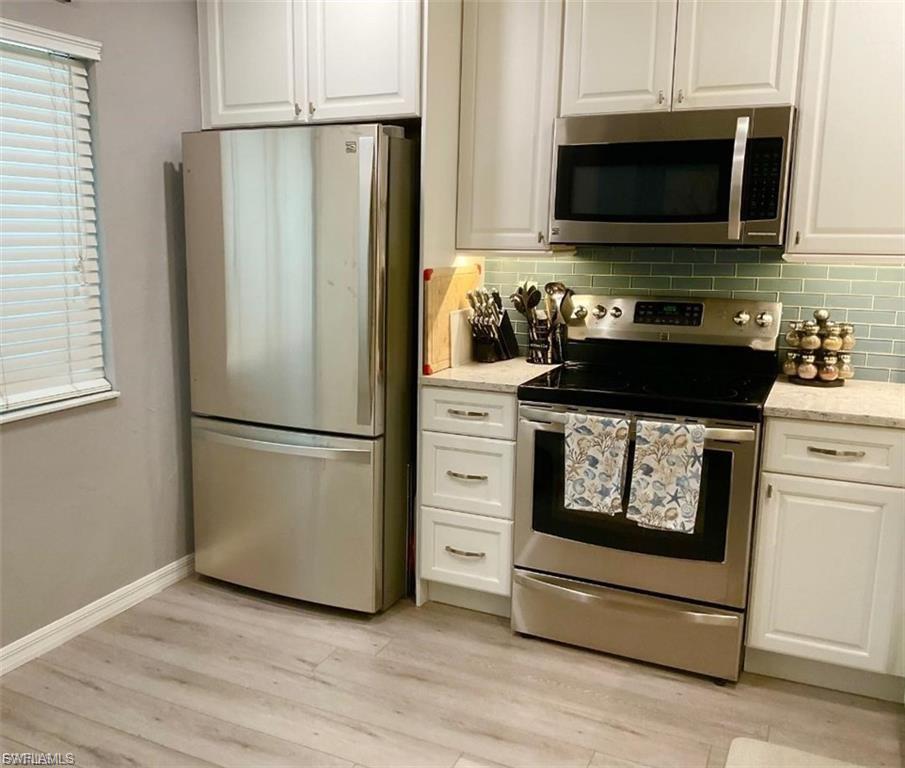 Kitchen featuring stainless steel appliances, light wood-finish flooring, white cabinetry, and a subway tile backsplash