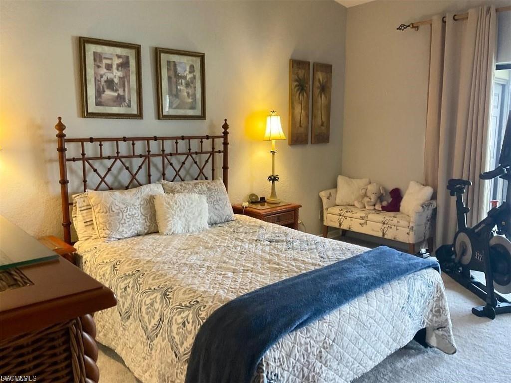 Textured wall finish, metal-frame bed, wood-finish nightstands, wall-to-wall carpeting, and neutral-toned drapes