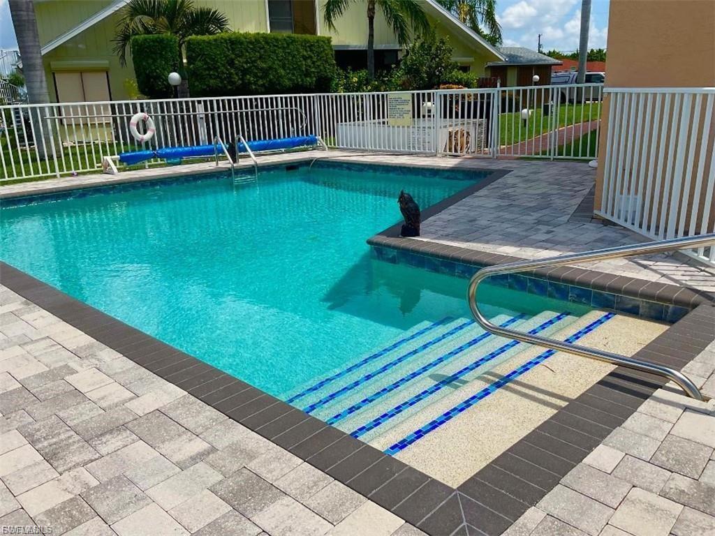 Swimming pool with integrated steps featuring blue mosaic tile accents, surrounded by a paver deck with a dark border, and enclosed by white fencing