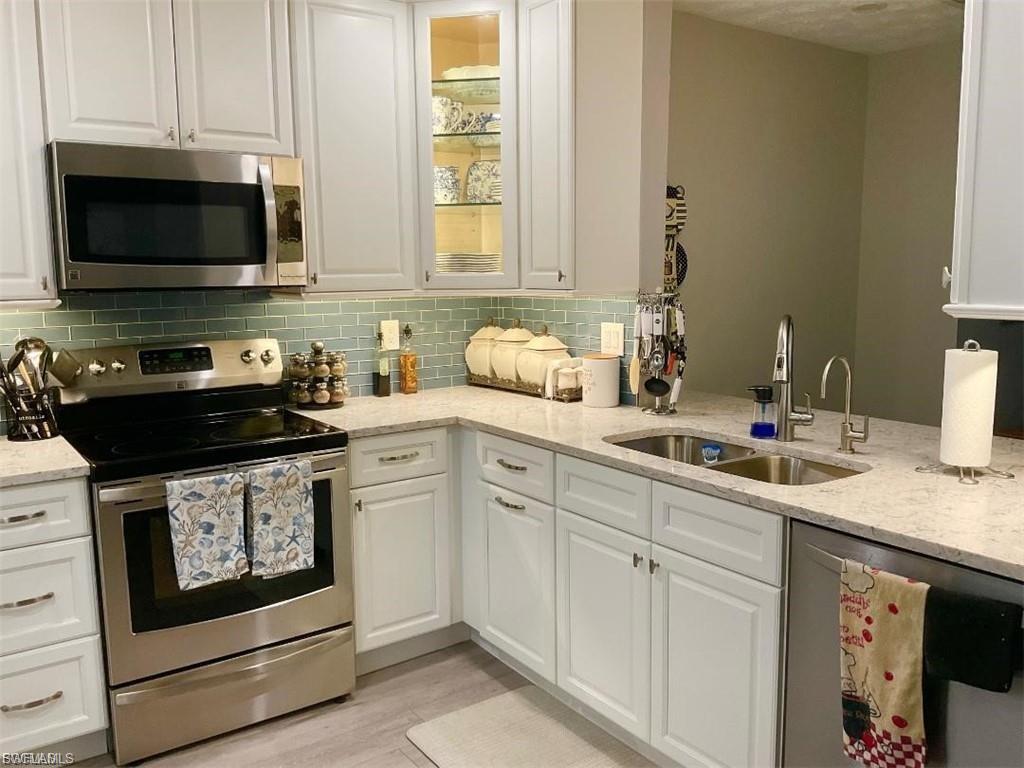 White cabinetry with brushed nickel hardware, stainless steel appliances, light-colored countertops, subway tile backsplash, and a double basin sink with a gooseneck faucet