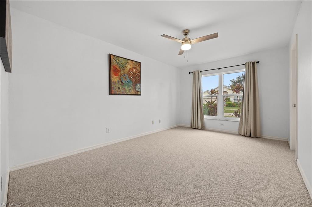 Neutral carpet flooring, white painted walls, large window with natural light, and a ceiling fan with integrated lighting