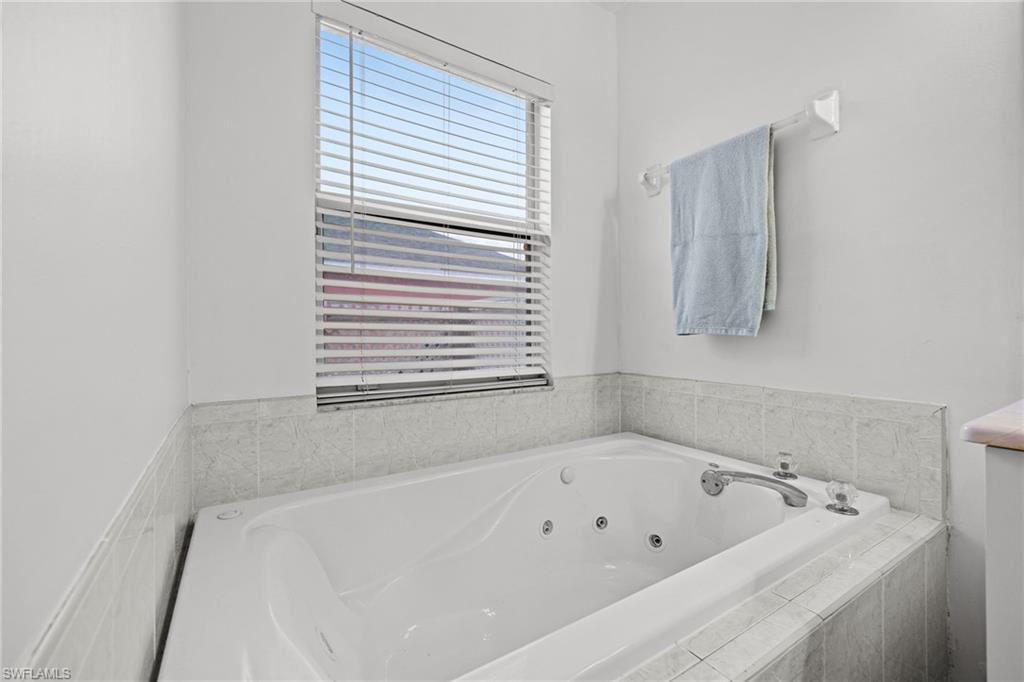 Spa-inspired primary bath featuring a deep soaking tub with integrated jets, tile surround, chrome fixtures, and a large window with privacy blinds
