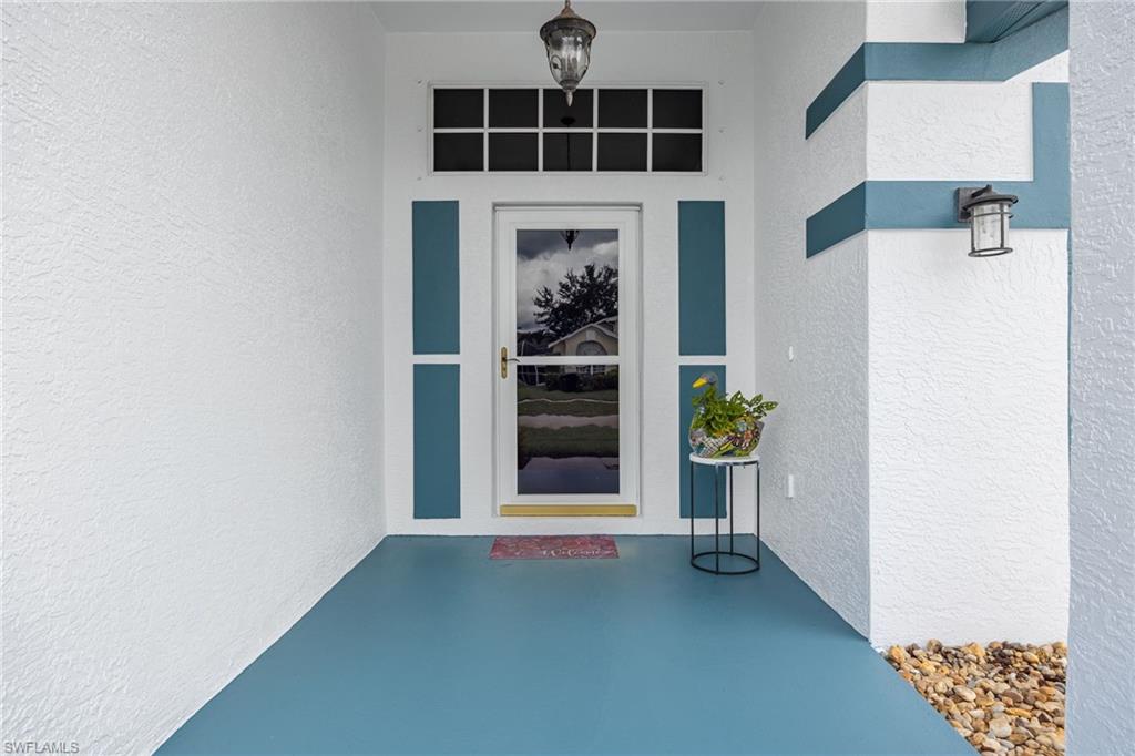 Welcoming entry featuring a teal-finished concrete floor, white stucco walls with teal trim accents, and a glass-paneled door with transom window detail