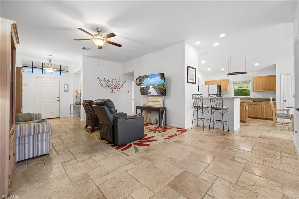 Open-concept living area featuring travertine tile flooring throughout, recessed ceiling lighting, and a ceiling fan