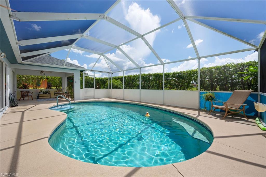 Screened-in pool deck featuring a freeform swimming pool with an integrated spa, concrete decking, and a covered lanai