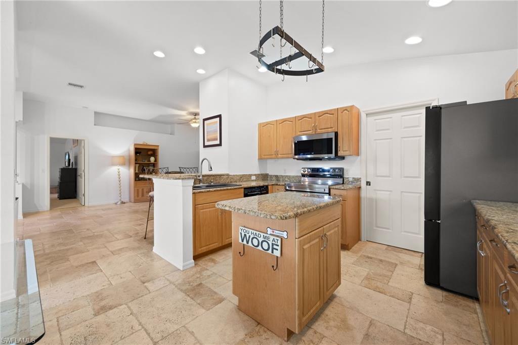 Spacious kitchen featuring wood-finish cabinetry, granite countertops, a large center island with seating, stainless steel appliances, and abundant recessed lighting throughout