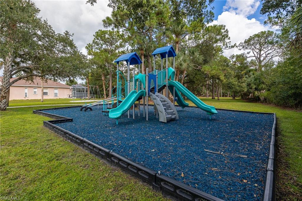 Outdoor play area featuring a multi-level playset with slides, swings, and a blue rubberized ground surface