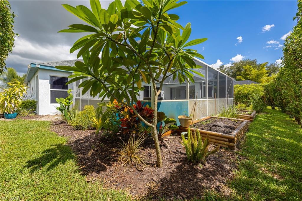 Expansive backyard oasis featuring mature tropical landscaping, raised garden beds, sparkling pool with screening enclosure, and lush lawn framed by established trees and verdant grounds