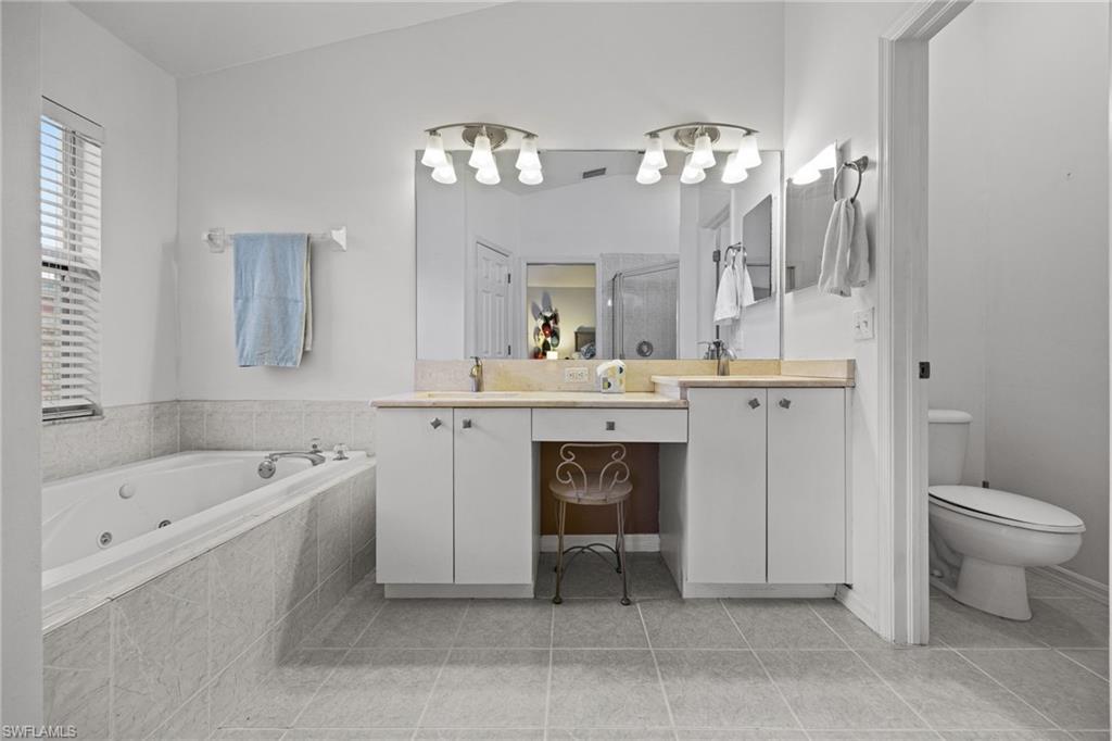Spa-inspired primary bathroom featuring dual vanities with wood-finish countertops, white cabinetry, and chrome fixtures