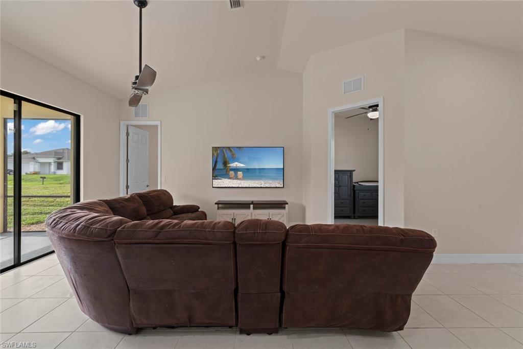 Vaulted ceiling with a ceiling fan, white tile flooring, and a sliding glass door leading to a screened lanai