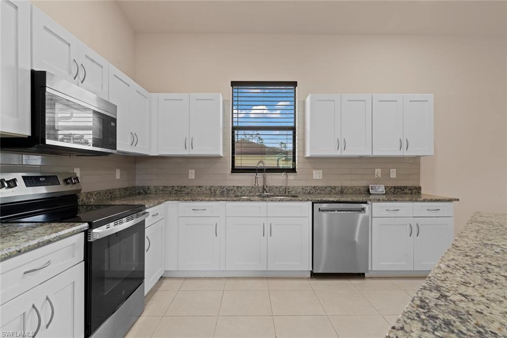 Kitchen featuring white cabinetry, granite countertops, stainless steel appliances, a tiled backsplash, and light-toned tile flooring
