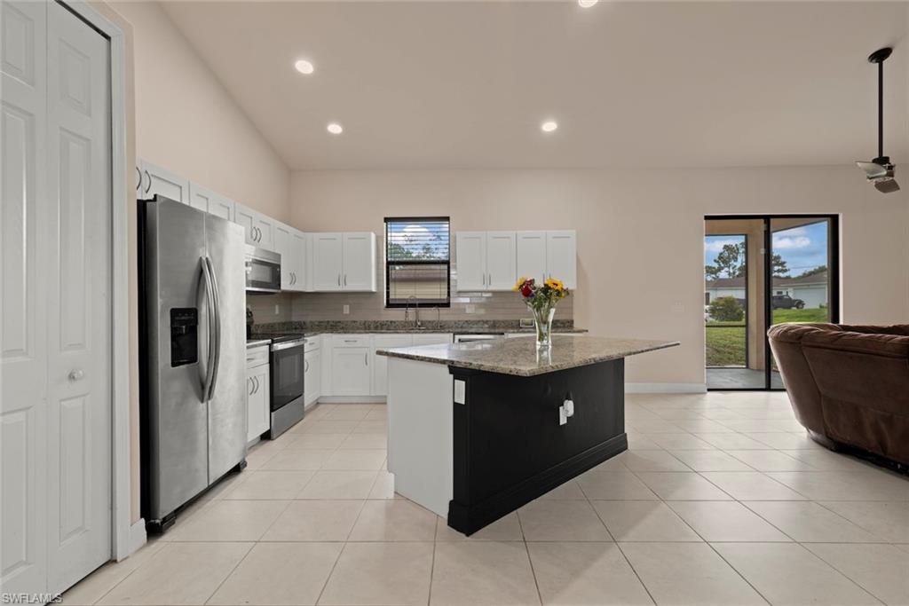 Kitchen featuring white cabinetry, stainless steel appliances, a granite countertop island, and tile flooring