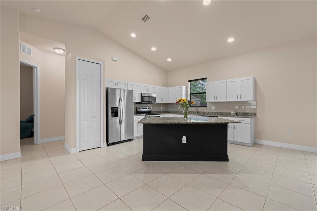 Vaulted ceilings, recessed lighting, white cabinetry, stainless steel appliances, and a central island with a contrasting base