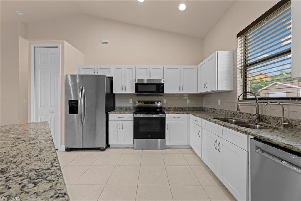 Kitchen featuring white cabinetry, granite countertops, stainless steel appliances, tiled flooring, and a vaulted ceiling