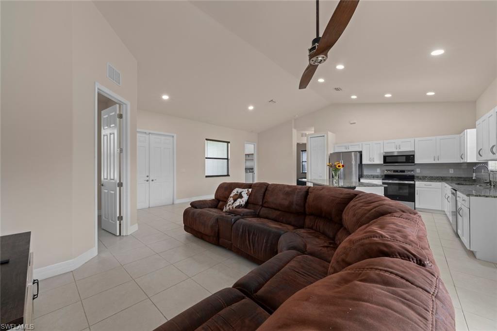 Vaulted ceilings with recessed lighting, tile flooring, and a kitchen featuring white cabinetry, stainless steel appliances, and granite countertops