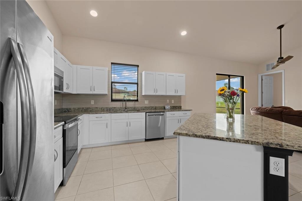 Kitchen featuring white cabinetry, stainless steel appliances, granite countertops, and tile flooring