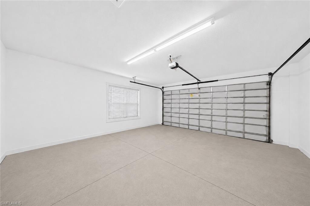Spacious garage featuring a light-toned concrete floor, window with horizontal blinds, overhead fluorescent lighting, and an automatic garage door opener