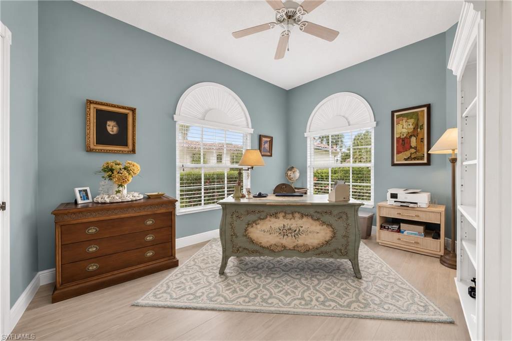 Vaulted ceiling with a ceiling fan, two arched transom windows with blinds, built-in shelving, and light wood-finish flooring