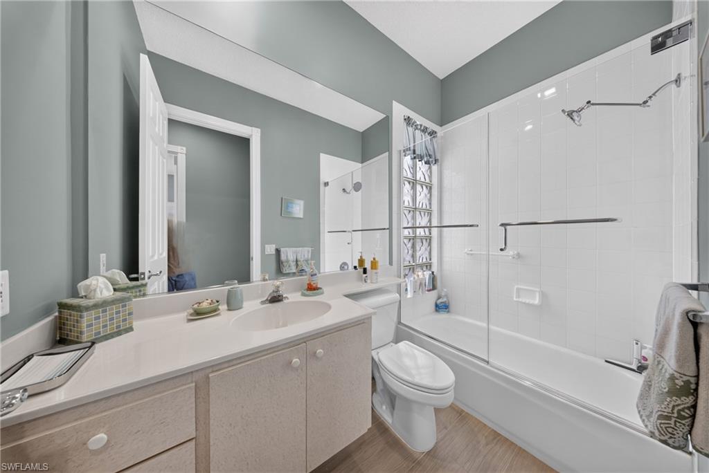 Bathroom featuring a vanity with an integrated sink, a large mirror, a shower-tub combination with glass block accents, wood-finish flooring, and light gray wall paint