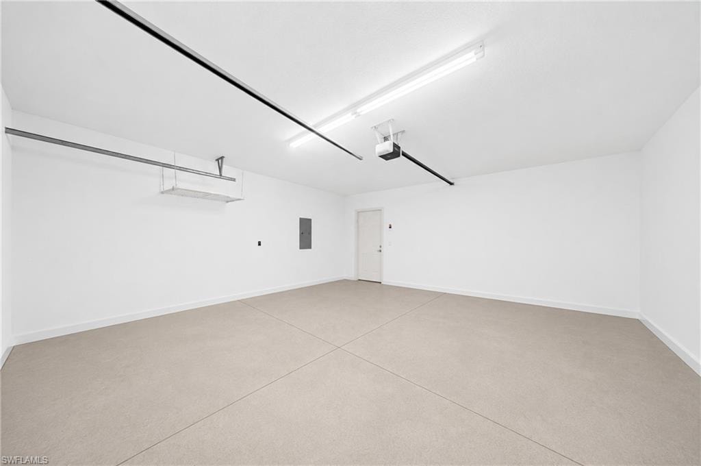 Spacious garage featuring a light-colored concrete floor, pristine white walls, and overhead fluorescent lighting