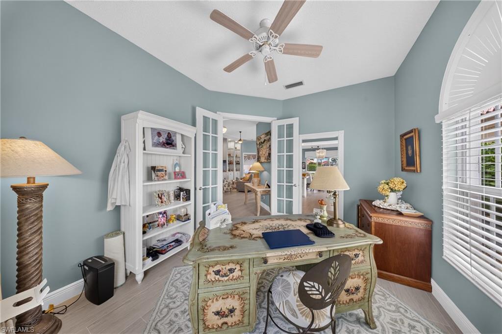 Office space featuring French doors, wood-finish flooring, a ceiling fan, and an arched window with plantation shutters