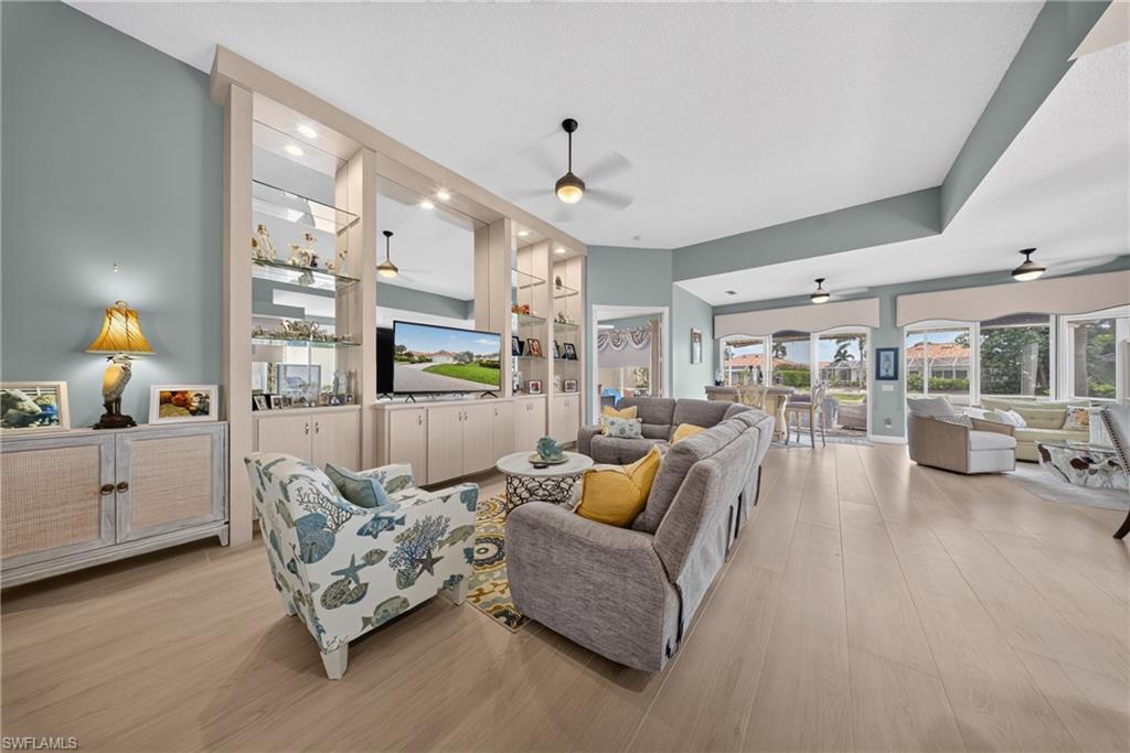 Spacious living area featuring light wood-finish flooring, a custom built-in entertainment center with integrated lighting, and multiple ceiling fans