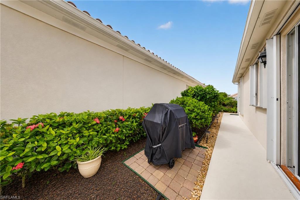 Exterior side yard featuring a stucco wall, mature shrubbery with pink blooms, and a paved walkway