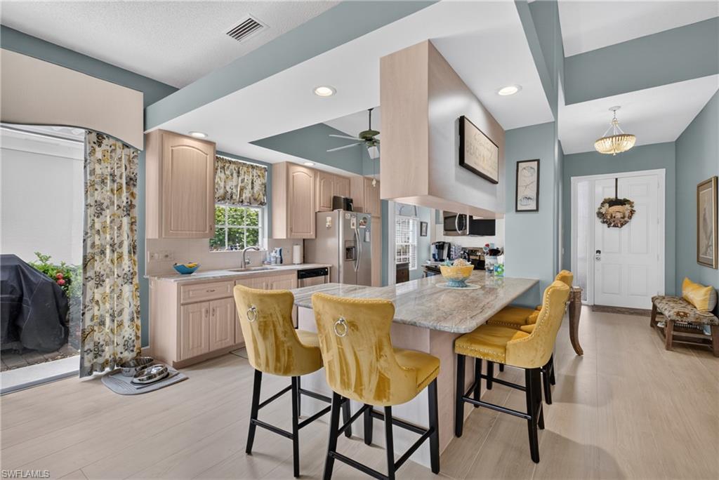 Kitchen featuring light wood-finish cabinetry, light stone-finish countertops, stainless steel appliances, and an expansive breakfast bar with seating