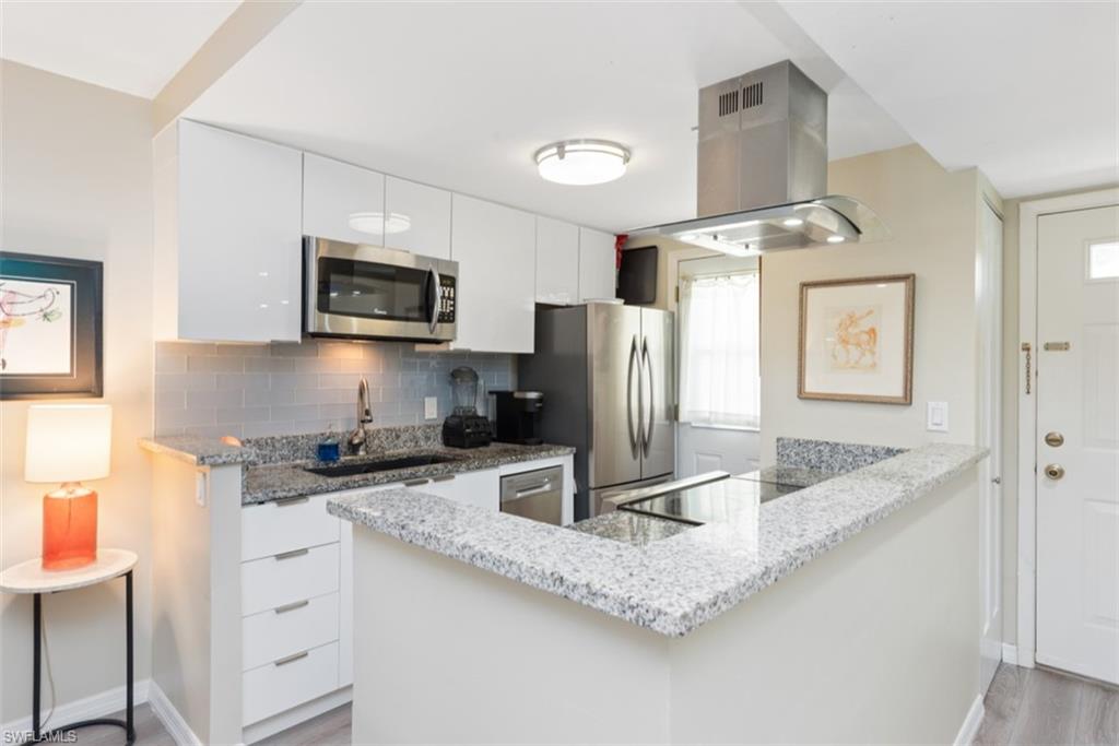 Kitchen with stainless steel appliances, decorative backsplash, white cabinets, island exhaust hood, and sink