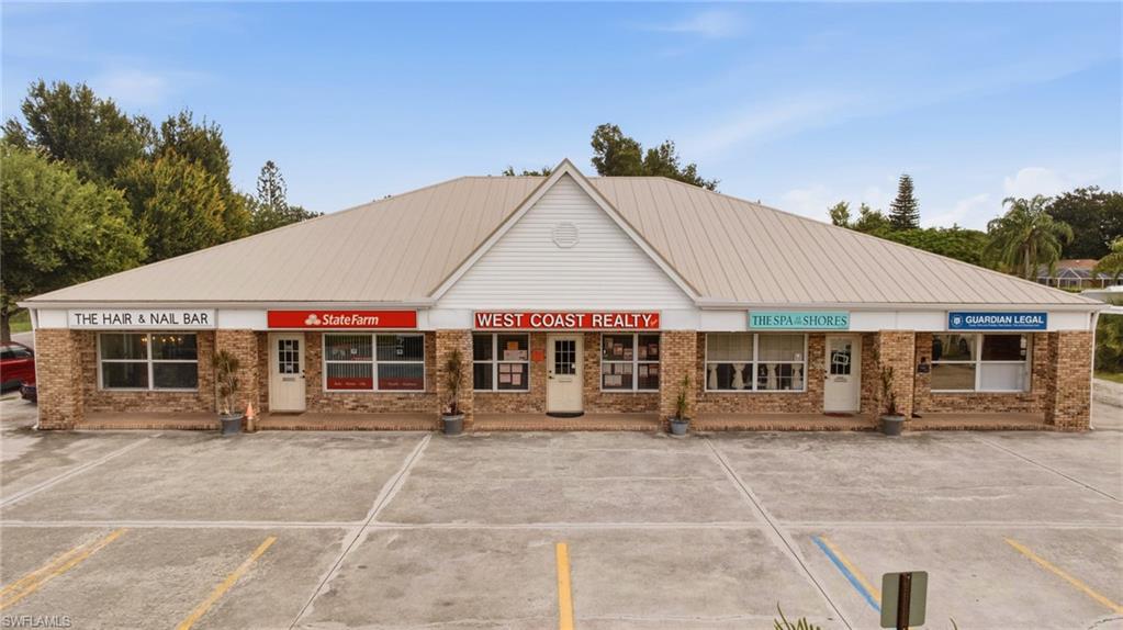 Commercial building featuring a metal roof, brick facade, storefront windows, multiple entry points, and a paved parking area