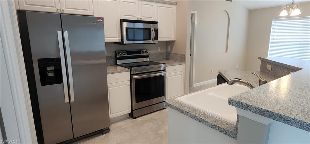 Kitchen with stainless steel appliances, white cabinets, light countertops, decorative light fixtures, and a Dining Room Chandelier