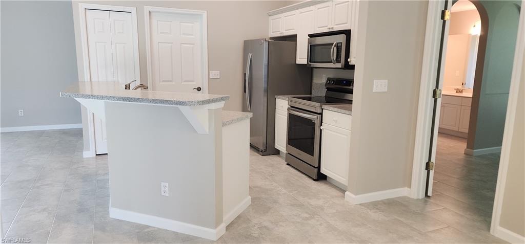 Open Kitchen with arched walkways, stainless steel appliances, light countertops, a kitchen island with sink, and white cabinetry