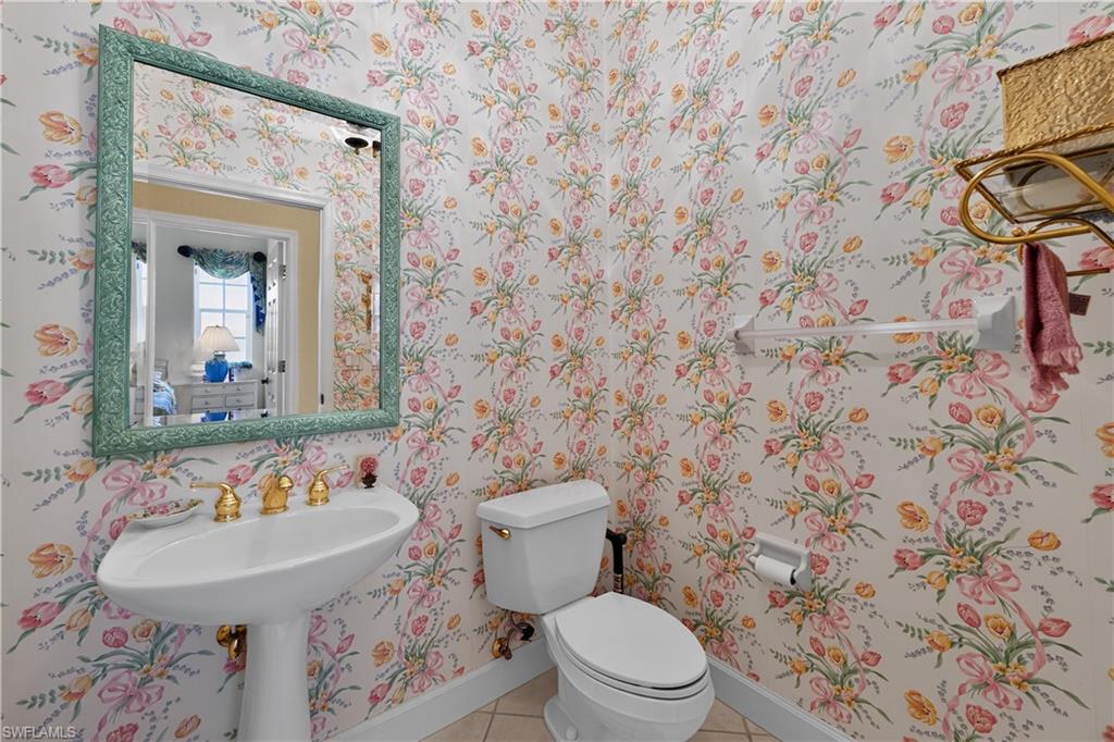 Pedestal sink with brass-finish faucet, framed mirror, floral-patterned wallpaper, and white toilet