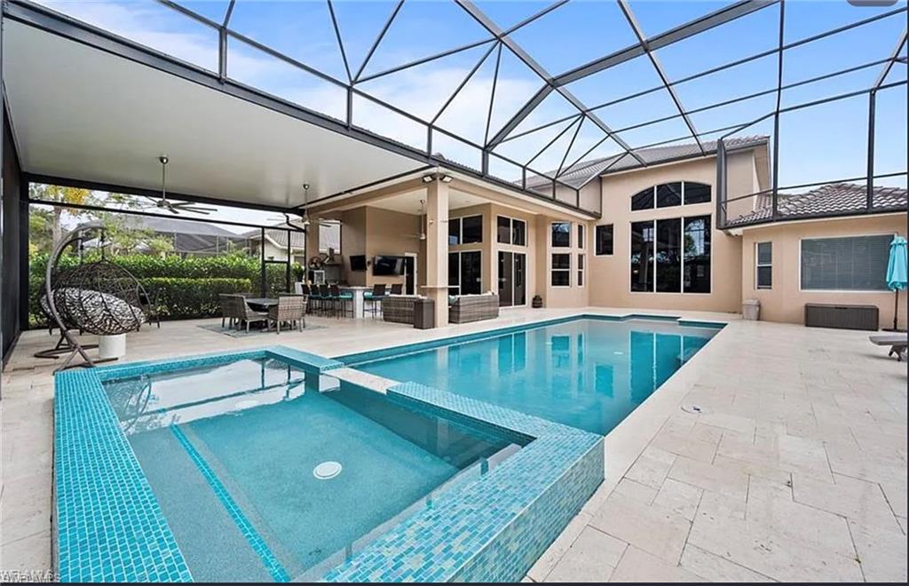 Screened outdoor living area featuring a large swimming pool, integrated spa with mosaic tile, covered lanai, and an exterior with multiple large windows
